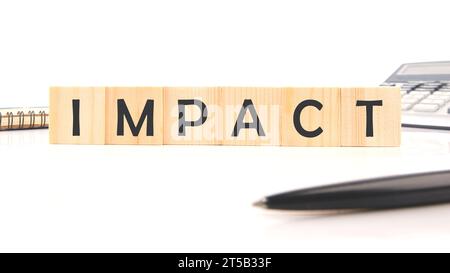 IMPACT word assembled from wooden cubes next to a calculator, pen and notepad Stock Photo