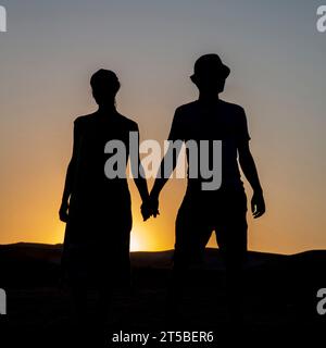 Silhouette of a romantic couple - A man and a woman standing in front of the sun and holding hands Stock Photo