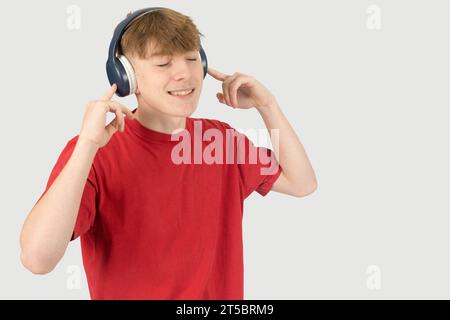 Caucasian 15 year old teenage boy, wearing a red t-shirt,  listening to music via headphones Stock Photo