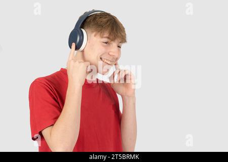 Caucasian 15 year old teenage boy, wearing a red t-shirt,  listening to music via headphones and smiling Stock Photo
