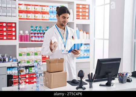 Young hispanic man pharmacist using touchpad holding pills bottle at pharmacy Stock Photo