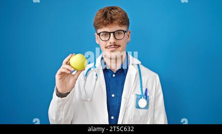 Young hispanic man doctor holding green apple over isolated blue background Stock Photo