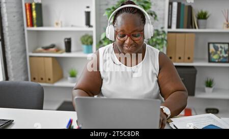 Brimming with success, this smiling african american boss-woman is slaying her business world. hunkered down in the office, jamming to music in headph Stock Photo