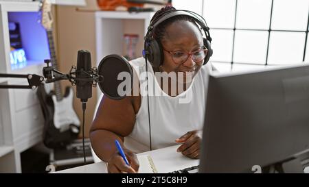 Smiling african american woman, a confident musician, composing a soulful song in a music studio, engrossed in her musical world. Stock Photo