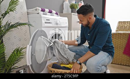 Young hispanic man doing laundry with washing machine at laundry room Stock Photo