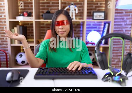 Middle age chinese woman wearing virtual reality glasses smiling cheerful presenting and pointing with palm of hand looking at the camera. Stock Photo