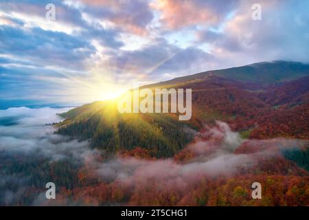 Fog spreads over the mountains at dawn. The sun rises on the horizon. Ukrainian Carpathians in the morning. Aerial drone view. Stock Photo