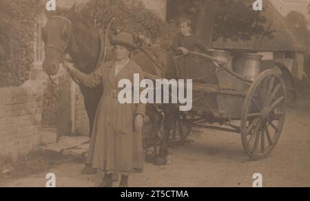 Milk round: First World War era photograph of a woman leading a horse and cart. The cart contains a small boy and several large milk churns for delivery Stock Photo