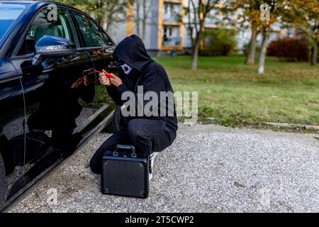 Attempted to steal a car using a suitcase in the city center - a thief in a hood with a mask on his face Stock Photo