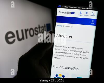 Person holding smartphone with webpage of EU institution European Statistical Office Eurostat in front of logo. Focus on center of phone display. Stock Photo