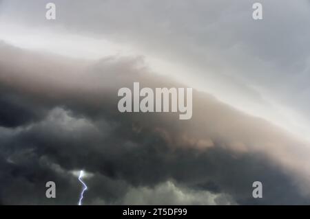 Looming dark storm clouds fill the sky, their ominous forms backlit by flashes of lightning. Stock Photo