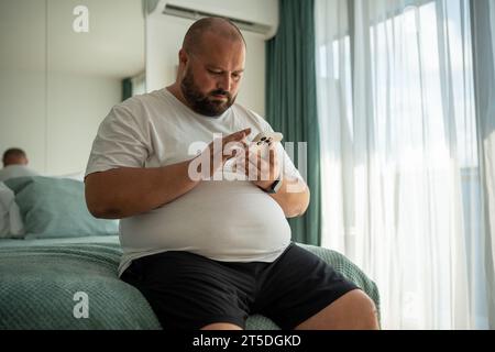 Fat bearded bald guy with smartphone chatting, dials number, types message, watches news, weather Stock Photo