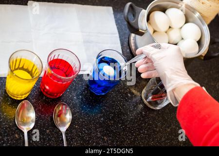 A woman dyes chicken eggs in multi-colored food dyes. Preparing for the feast of the holy Easter. Stock Photo