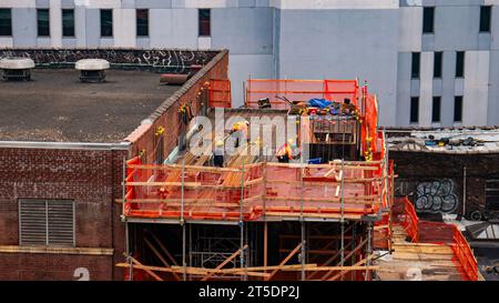 Construction workers on orange scaffolding on an urban city building Stock Photo