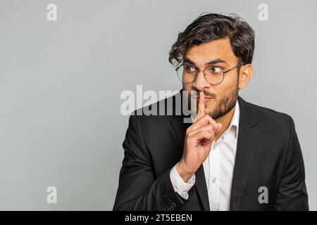 Shh be quiet please. Indian businessman presses index finger to lips makes silence gesture sign do not tells secret, stop talk gossip, confidential privacy. Arabian man guy isolated on gray background Stock Photo