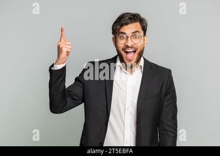 Eureka. Inspired Indian businessman pointing finger up with open mouth, having good idea, plan, startup, showing inspiration motivation gesture, problem solution. Arabian man on gray background Stock Photo