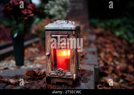 Ornate metal grave lantern with a burning candle on a grave with autumn leaves on All Saints' Day Stock Photo