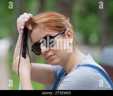 Blind red-haired woman sitting outdoors leaning on a cane.  Stock Photo