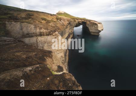 A stunning landscape featuring an imposing arch situated on a rugged cliff. Tunnel Beach, New Zealand Stock Photo