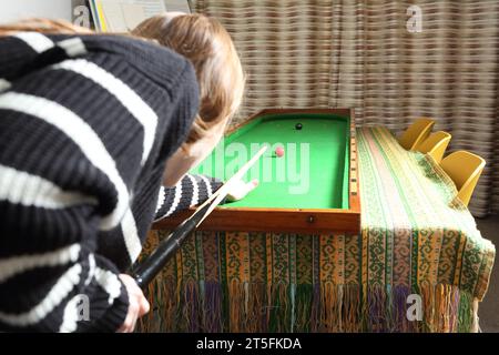 Teenage girl playing traditional pub game of bagatelle in lounge at home - view from her viewpoint over the shoulder. Stock Photo