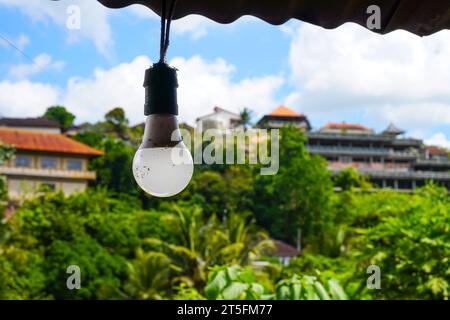 White hanging light bulbs against a backdrop of green trees and traditional buildings Stock Photo