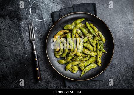 Stir-fried green Edamame Soy Beans with sea salt and sesame seeds in a plate. Black background. Top view. Stock Photo