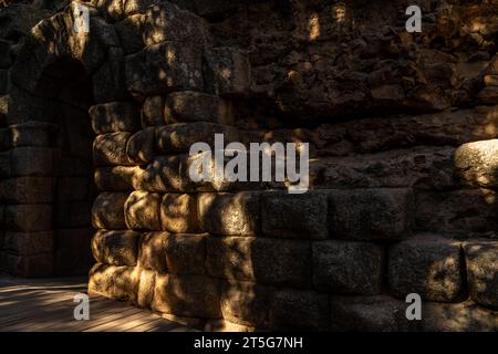 Roman rock wall surrounding the steps of the ancient Roman Theater in Mérida, with the arched door in the background illuminated by dawn sunlight betw Stock Photo