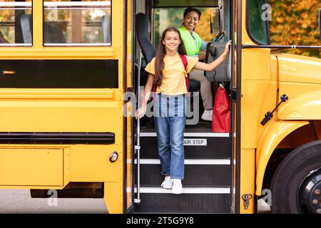 Happy preteen girl getting of the yellow school bus, smiling at camera Stock Photo