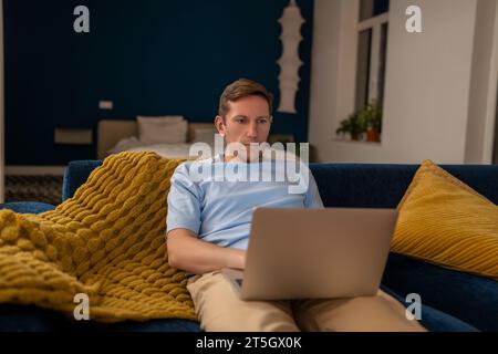 Man sit on couch with laptop on lap studying, relaxing, chilling, browsing Internet, checking news Stock Photo