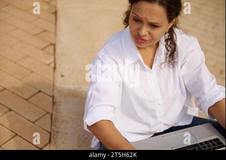 Close-up portrait of mixed race young adult woman expressing sadness failing business tender project, desperately and thoughtfully looking aside, sitt Stock Photo