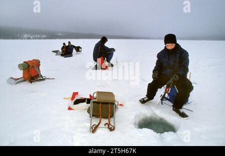 TROMSO,NORWAY - JANUARY 14 2022: Fishermen ice fishing on a frozen lake in winter with fishing pole or rod, ice auger and equipment for fishing Stock Photo