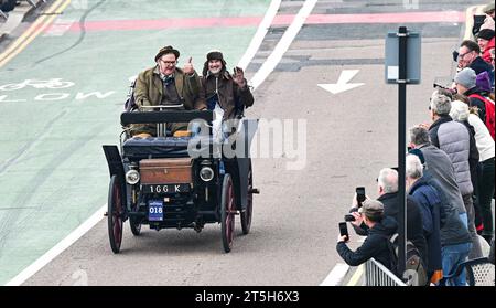 Brighton  UK 5th November 2023 -  Participants in an 1898 Rochet-Schneider wave to the crowds on Brighton seafront during this years RM Sotheby's London to Brighton Veteran Car Run commemorating the famous Emancipation Run of November 1896.  : Credit Simon Dack / Alamy Live News Stock Photo