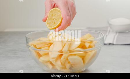 Apple slices in a glass bowl. Topping slices with lemon juice. Apple cake recipe, woman hands Stock Photo