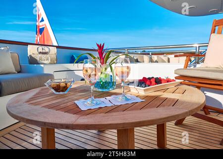 Two glasses of rose wine on a round teak table with a bowl of blueberries, raspberries and strawberries on the sundeck of a charter yacht. Stock Photo