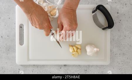 Woman hands peeling and cutting fresh garlic. Close-up preparation process, view from above Stock Photo