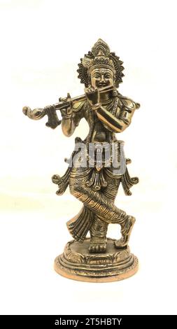 lord krishna playing flute music, an avatar of vishnu god of hindu religion, shiny bronze statue with a crown and ornamental details isolated Stock Photo