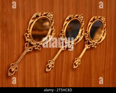 three vintage round golden hand mirrors crafted in bronze kept for display on a wooden wall inside a traditional handicraft and souvenir shop Stock Photo