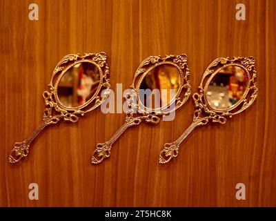 three vintage round golden hand mirrors crafted in bronze kept for display on a wooden wall inside a traditional handicraft and souvenir shop Stock Photo