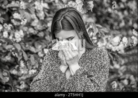 Pollen allergy, girl sneezing. Allergy, sneezing, spring. Woman sneezing in front of blooming tree. Black and white Stock Photo