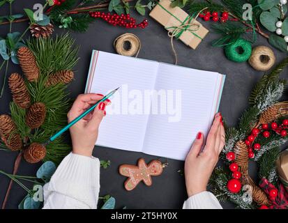 A woman sits at a table surrounded by Christmas decorations and gifts. She writes in a notepad, top view Stock Photo