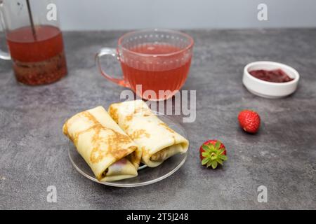 pancakes with berry filling and strawberries, a cup of fruit tea, on a dark gray table. Stock Photo