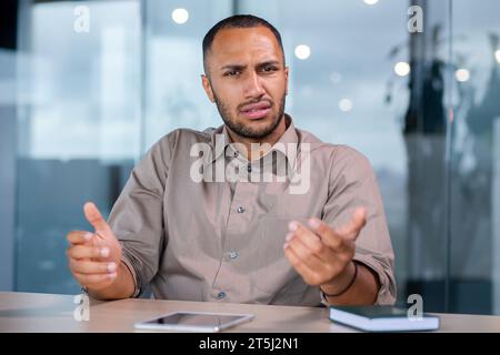 Upset disappointed and sad looking at web camera, man unhappy on online video meeting sitting at table inside office at workplace. Stock Photo