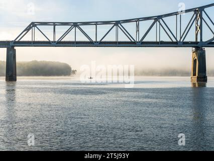 Fisherman in water of Upper Mississippi on calm misty morning by Julien Dubuque Bridge Stock Photo