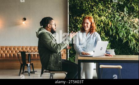 Happy coworkers collaborate in a vibrant cafe. Discussing, smiling, and working together using laptops, they create a positive and productive office e Stock Photo