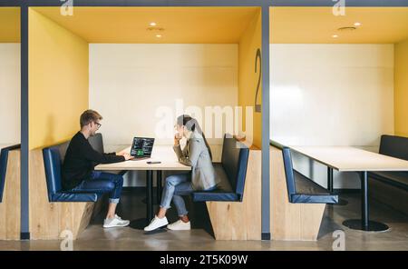 Colleagues in a coworking office discuss a software design and programming project. Coding experts working remotely, using a laptop. Teamwork drives e Stock Photo