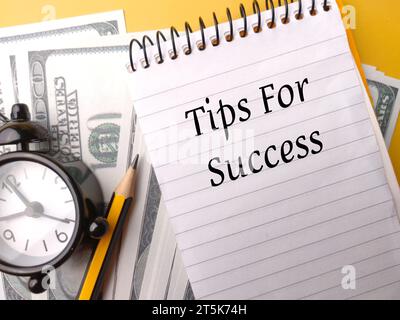 Alarm clock,pencil and banknotes with text Tips For Success on yellow background Stock Photo