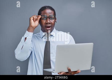 young african american man on a gray background looking at a laptop in surprise Stock Photo
