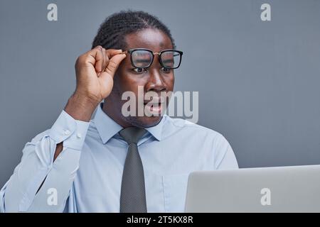young african american man on a gray background looking at a laptop in surprise Stock Photo