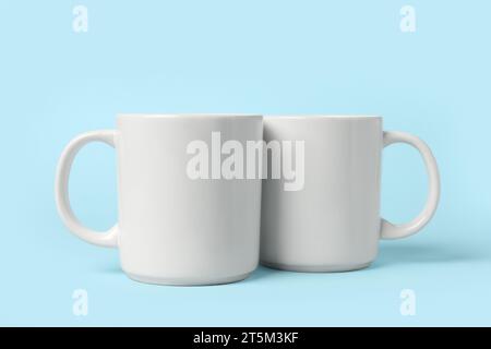 Two white ceramic mugs on light blue background Stock Photo