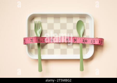 Empty tray plate and fork, spoon with tape measure on pink table background. healthy diet body weight control concept Stock Photo